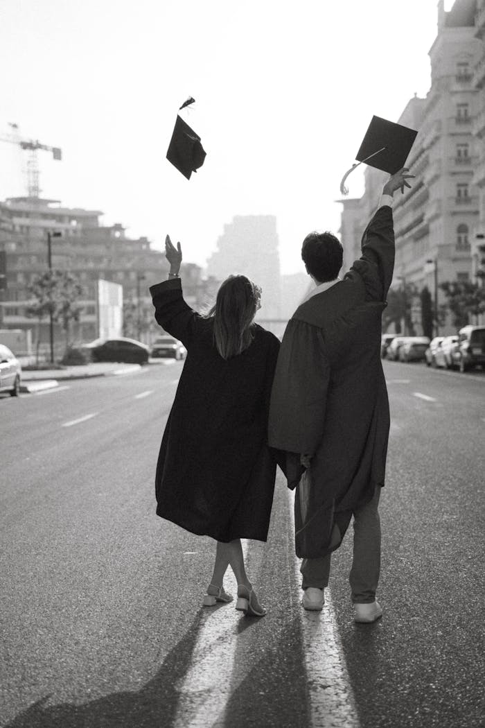 Two graduates in gowns celebrate by tossing caps on a city street, symbolizing achievement.